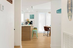 A modern kitchen with a wooden island, a dining area with chairs, and a sign that says 'BEACH CALLING'.