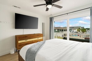 A bedroom with a bed, a wooden dresser, a flat-screen TV, and a ceiling fan.