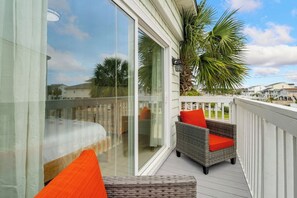 A balcony with wicker furniture, a glass door, and a view of palm trees and houses.