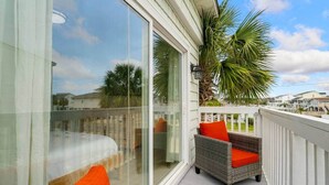 Een balkon met een glazen deur, rieten meubilair en uitzicht op palmbomen en huizen.