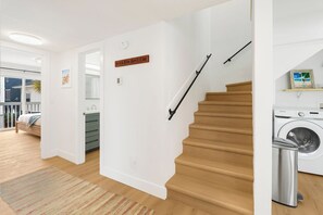 Una escalera con acabados de madera, un área de lavandería con lavadora, y una cama con vistas al exterior.