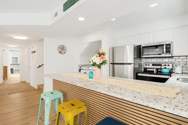 Una cocina moderna con gabinetes blancos, electrodomésticos de acero inoxidable y una isla de madera con taburetes.
