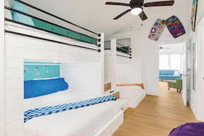 A bunk bed room with a ceiling fan, a blue sofa, and a green chair in the background.