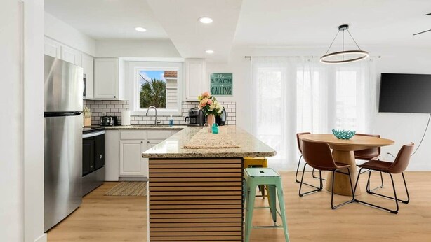 Een moderne keuken met witte kastjes, een roestvrijstalen koelkast, een houten kookeiland en een eethoek met een ronde tafel en stoelen.