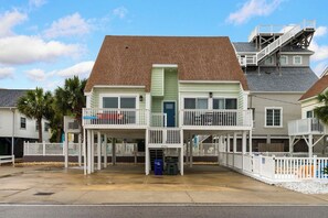 A beachfront property with a two-story building, a covered porch, and a staircase leading to a balcony.