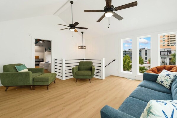 A modern living room with a sofa, armchairs, and a ceiling fan.