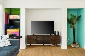 A living room with a flat-screen TV, a colorful arcade machine, a blue sofa, and a small plant.