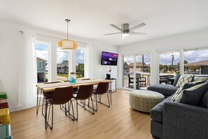 A modern living room with a dining area, large windows, a ceiling fan, and a flat-screen TV. - Beach Buddies 2 is 3 bed/2 bath with pool (North Myrtle Beach)