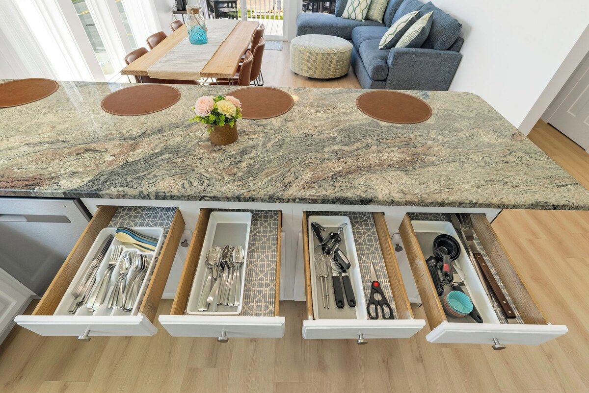 A kitchen with a marble countertop, multiple drawers for utensils, and a dining area with a table and chairs.