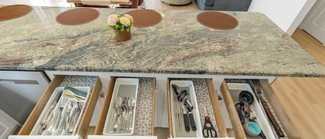 A kitchen with a marble countertop, multiple drawers for utensils, and a dining area with a table and chairs.