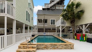 A swimming pool with a stone border, surrounded by white railings and a palm tree. - Beach Buddies 2 w/pool (North Myrtle Beach)