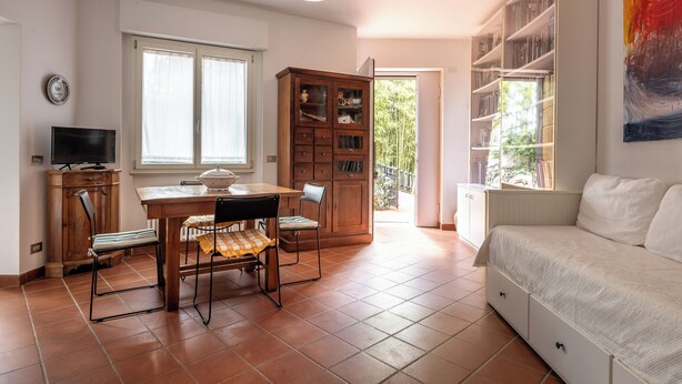 Una sala de estar con un sofá, una mesa de comedor con sillas, un televisor, una estantería y un ventanal grande.