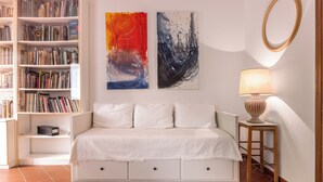Una sala de estar moderna con un sofá blanco, una estantería, dos cuadros abstractos, un espejo redondo y una lámpara sobre una mesita de madera.