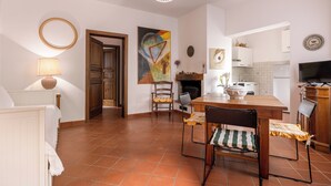 Amplia sala de estar con mesa y sillas de madera, chimenea y cocina al fondo.