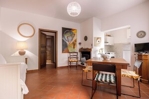 Amplia sala de estar con mesa y sillas de madera, chimenea y cocina al fondo.