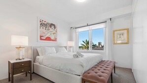 A bedroom with a bed, bedside tables, a bench, a window with a view, and artwork on the walls. - Elegance in Darling Point (Darling Point)