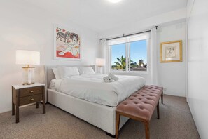 Ein Schlafzimmer mit einem Bett, Nachttischen, einer Bank, einem Fenster mit Ausblick und Kunstwerken an den Wänden.