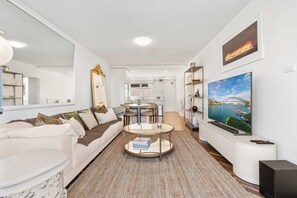 Ein modernes Wohnzimmer mit Sofa, Couchtisch, Fernseher und einer Küche im Hintergrund.