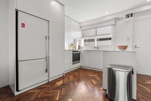 A modern kitchen with white cabinetry, a stainless steel refrigerator, and a herringbone wood floor. - Elegance in Darling Point (Darling Point)