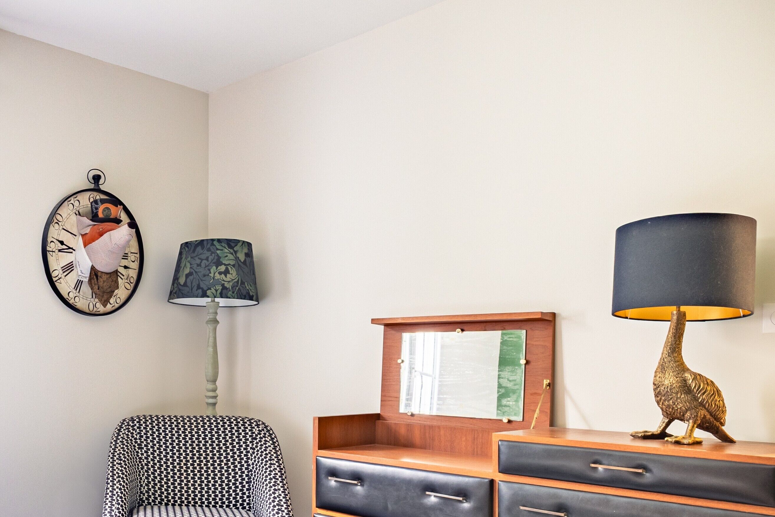 A room with a clock, a lamp, a cabinet, and a chair.