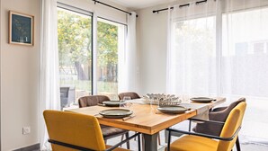 Un comedor con una mesa de madera, sillas amarillas y vistas a un jardín a través de amplios ventanales.
