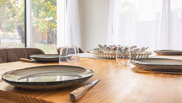 Una mesa de comedor con platos, cubiertos y vasos, en una habitación con ventana y cortinas.