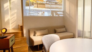 A modern room with a sofa, a small table with a lamp, a window with a view of a building, and a projection of 'Autumn Playlist' on the wall. - Mullaejung (Seoul)