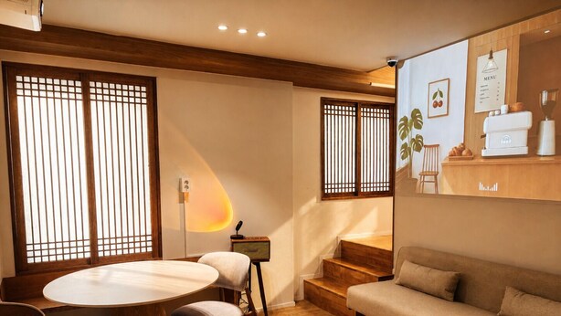 A modern living room with a round wooden table, a sofa, and a staircase. - Mullaejung (Seoul)