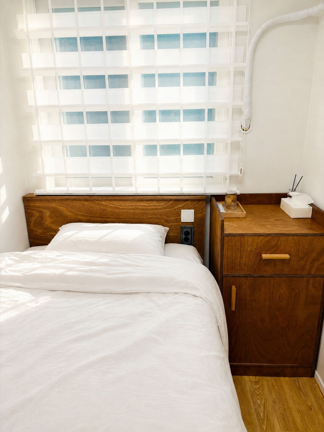 A bedroom with a wooden headboard, a bedside table with a lamp, and a window with blinds.