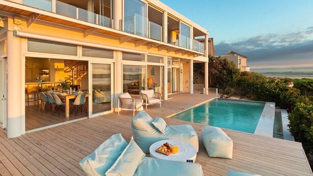 A modern house with a pool, outdoor dining area, and a view of the landscape. - Mbizi Lagoon House (Hermanus)