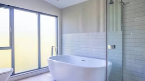 Ein modernes Badezimmer mit freistehender Badewanne, einer Duschkabine aus Glas und einem großen Fenster für natürliches Licht.