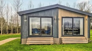 Eine moderne, eingeschossige Hütte mit großen Schiebeglastüren, einer Holzterrasse und einem Rasen.