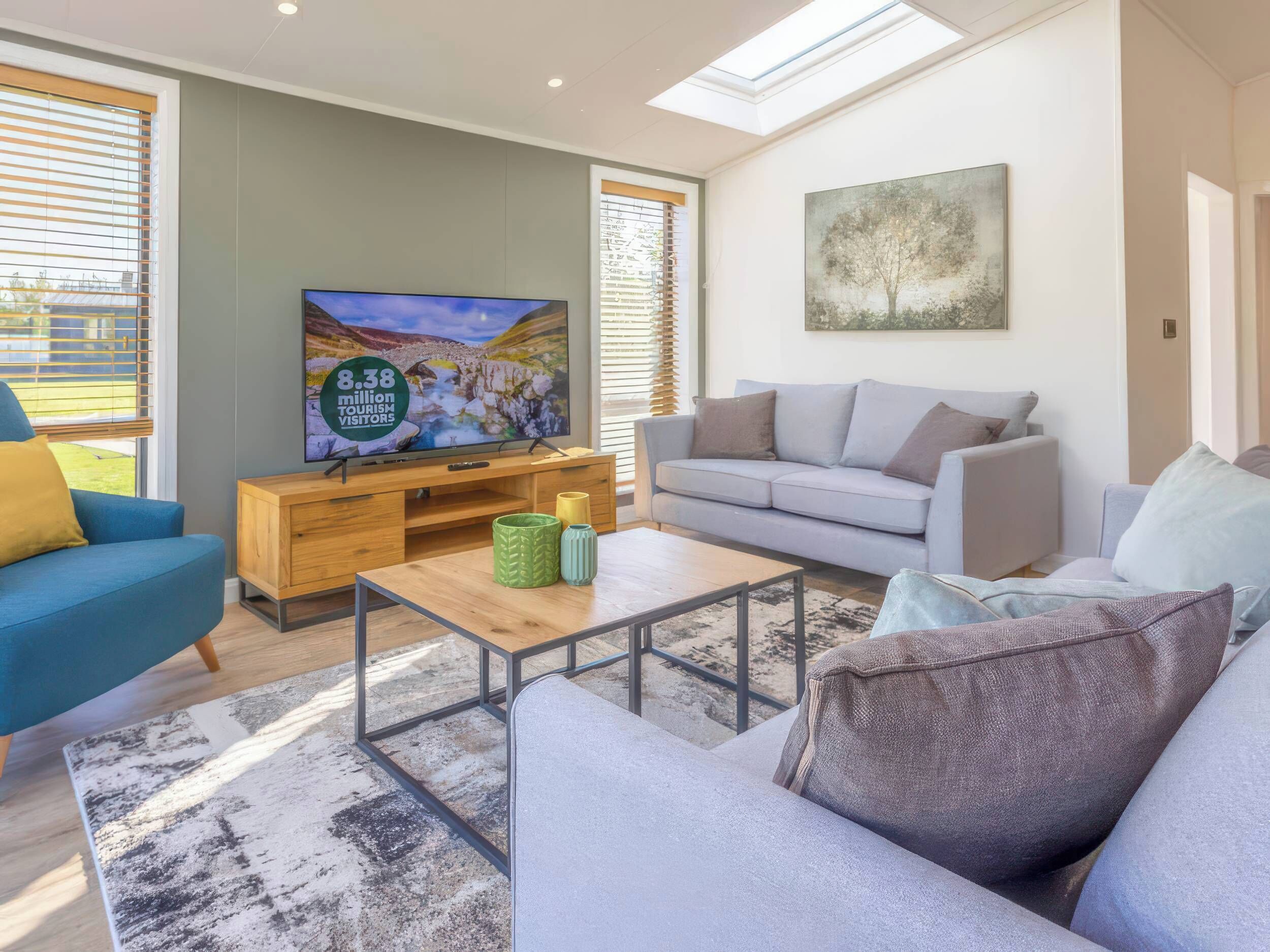 A modern living room with a flat-screen TV, grey sofa, blue armchair, and a coffee table with decorative vases.
