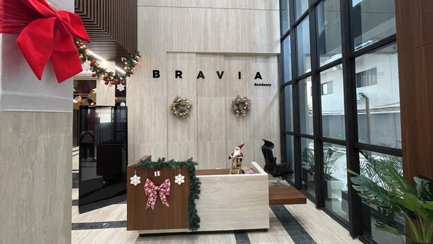 A modern lobby with a reception desk, a large red bow decoration, and the word "BRAVIA" on the wall.