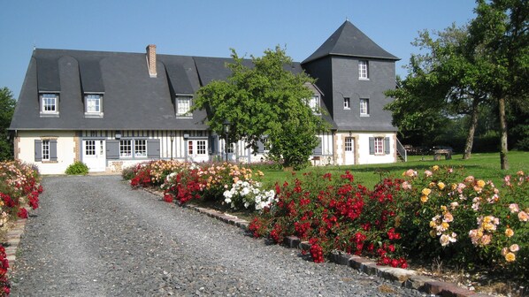 A large house with a gravel driveway, surrounded by a well-maintained garden with various flowers.