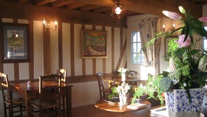 A dining area with wooden furniture, a painting on the wall, and a potted plant on the table. - Blue Azur Guest Room with Shared Terrace & Garden, Wi-Fi (Honfleur)
