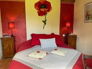 A bed with red and white bedding, two red flower pillows, a white pillow, and a wall with a red flower painting. - Guest Room 'Red Poppies' with Shared Terrace, Garden, and Wi-Fi (Honfleur)