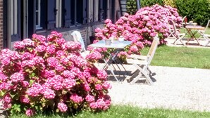 A building with a covered porch, outdoor seating, and pink flowering plants. - “Coquelicots Rouges” Guest Room with Shared Terrace & Garden, Wi-Fi (Honfleur)