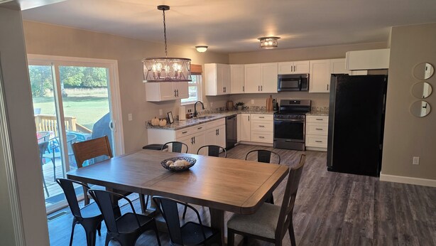 A modern kitchen with white cabinets, a stainless steel refrigerator, and a dining area with a wooden table and chairs. - New Home with Game Room and Nature Trails in Port Huron (Port Huron)