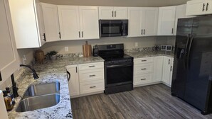A kitchen with white cabinets, a black refrigerator, a stainless steel sink, and a granite countertop. - New Home with Game Room and Nature Trails in Port Huron (Port Huron)