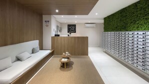 A modern reception area with a wooden reception desk, a green wall, and a row of mailboxes. - Mobi One Paulista (São Paulo)