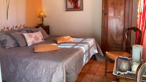 A bedroom with a bed, pillows, a nightstand, a lamp, a wooden door, and a chair.