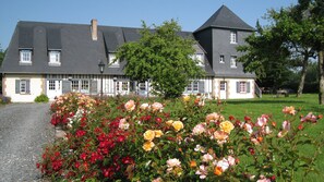 A large, two-story house with a prominent chimney, a well-maintained garden with various flowers, and a paved driveway. - Les Arums Guest Room with Shared Terrace, Garden, and Wi-Fi (Honfleur)