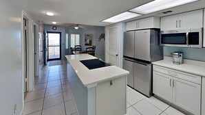 A modern kitchen with white cabinets, a stainless steel refrigerator, a microwave, and a coffee maker. - Windjammer 215 | Balcony Views + Resort Amenities (St. Augustine)