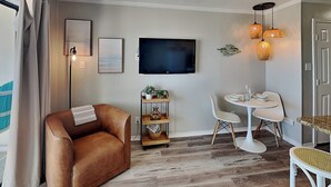 Un salon moderne avec un canapé en cuir, un téléviseur à écran plat, une table à manger avec des chaises et une petite étagère avec des plantes.