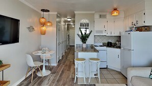 Une cuisine moderne avec des meubles blancs, un coin repas avec des chaises blanches et un îlot central doté de tabourets.