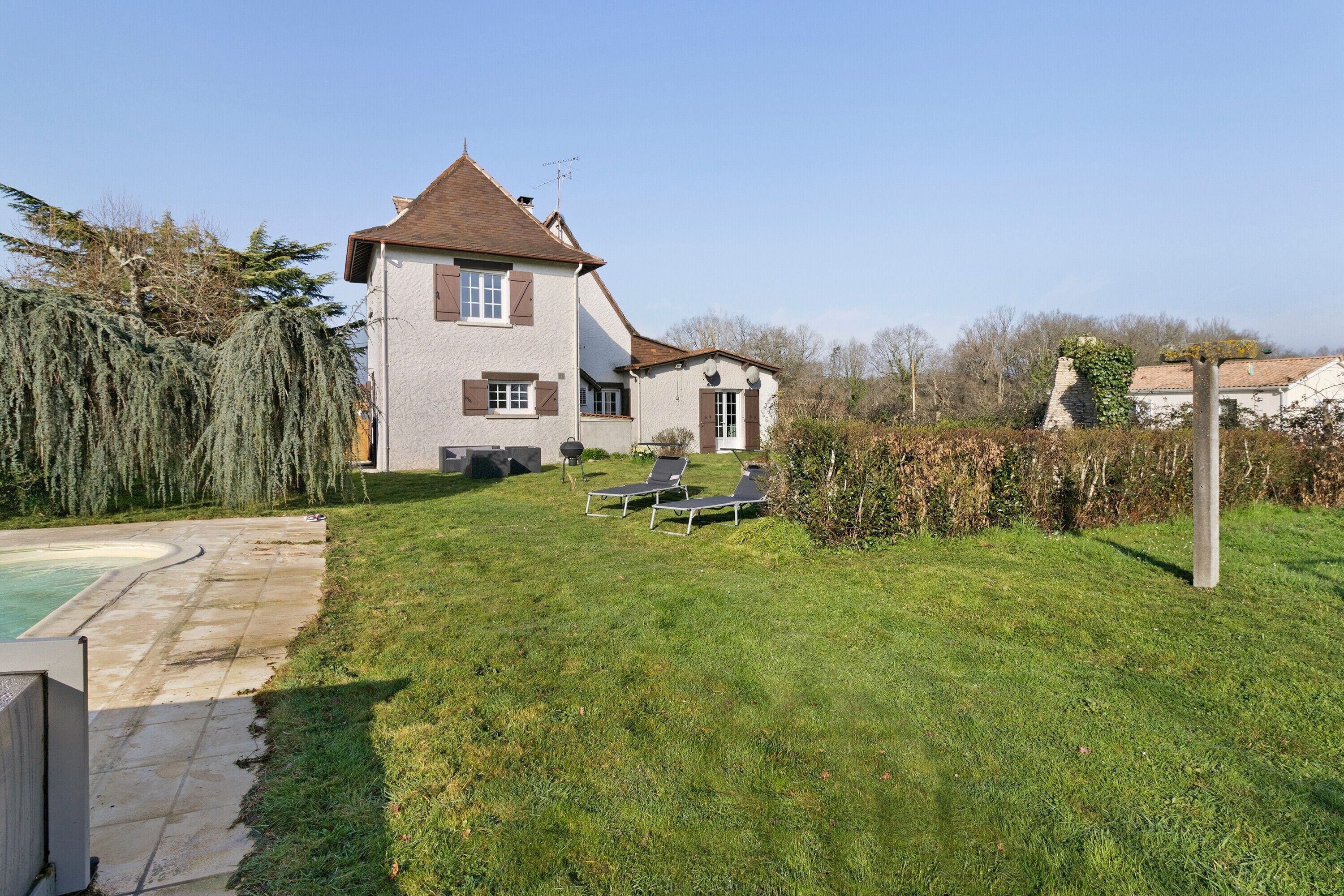 A two-story house with a swimming pool, a small garden, and a patio with two sun loungers.