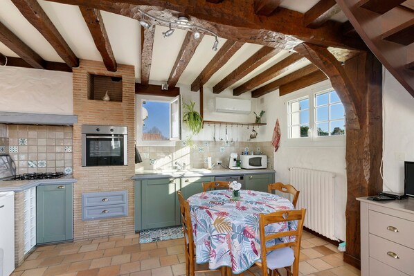 Une cuisine équipée d’une cuisinière à gaz, d’un four, d’un four à micro-ondes et d’un coin repas avec une table et des chaises.