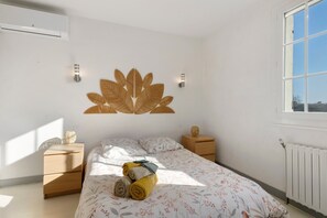 Une chambre à coucher comprenant un lit, deux tables de chevet, un luminaire fixé au mur, un radiateur et une fenêtre.