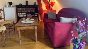A cozy living room with a wooden coffee table, a red sofa, a bookshelf, and a small table with decorative items. - “Romantic Suite” Guest Room with Shared Terrace & Garden, Wi-Fi (Honfleur)